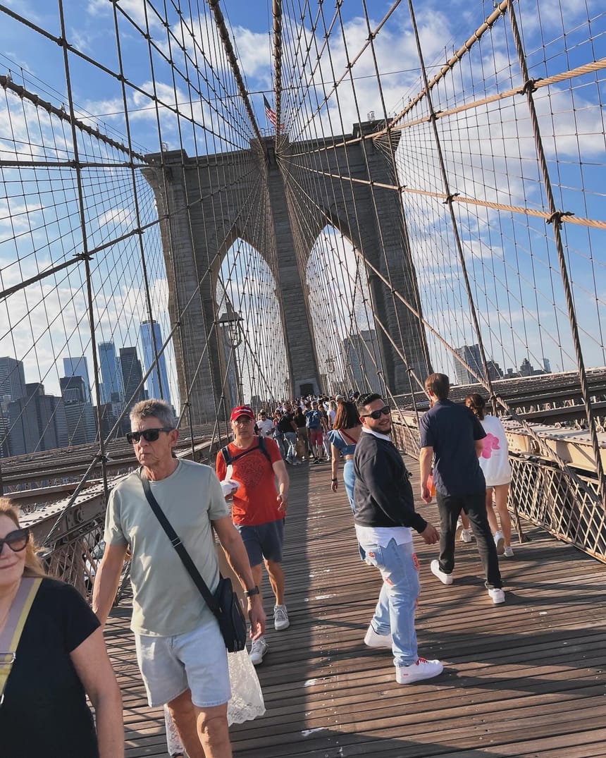 Cristian caminando por el Puente de Brooklyn entre la gente, mirando hacia atrás